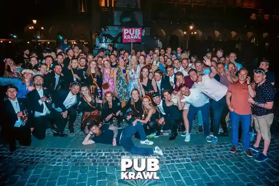 A large group of people poses together at night in front of a "PUB KRAWL" sign on a cobblestone street. Most are dressed up and appear to be enjoying a social event.