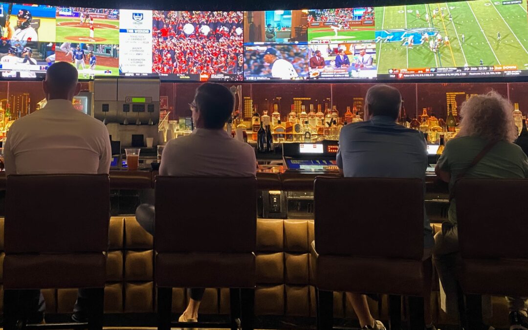 Three people seated at a Sports Bar in Krakow, watching multiple sports games on large tv screens.
